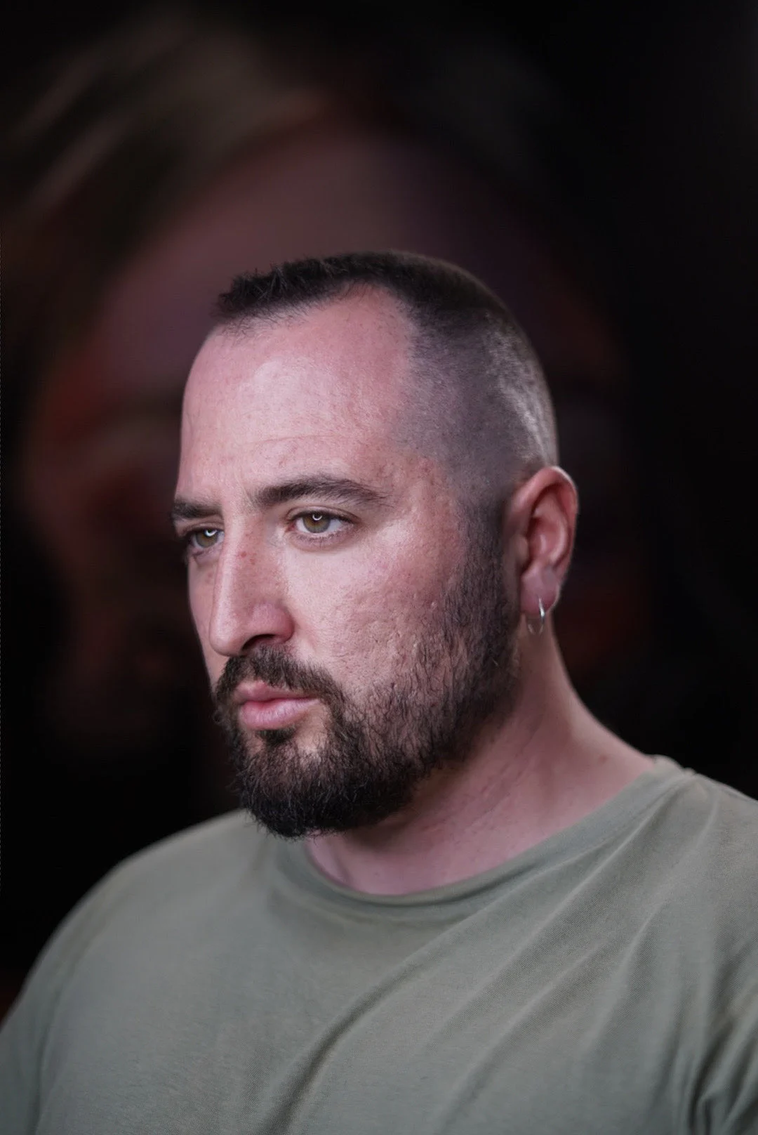 Portrait of Ahmet Özaydın, the tattoo artist known as BORZ, in a sage-green T-shirt against a dark background