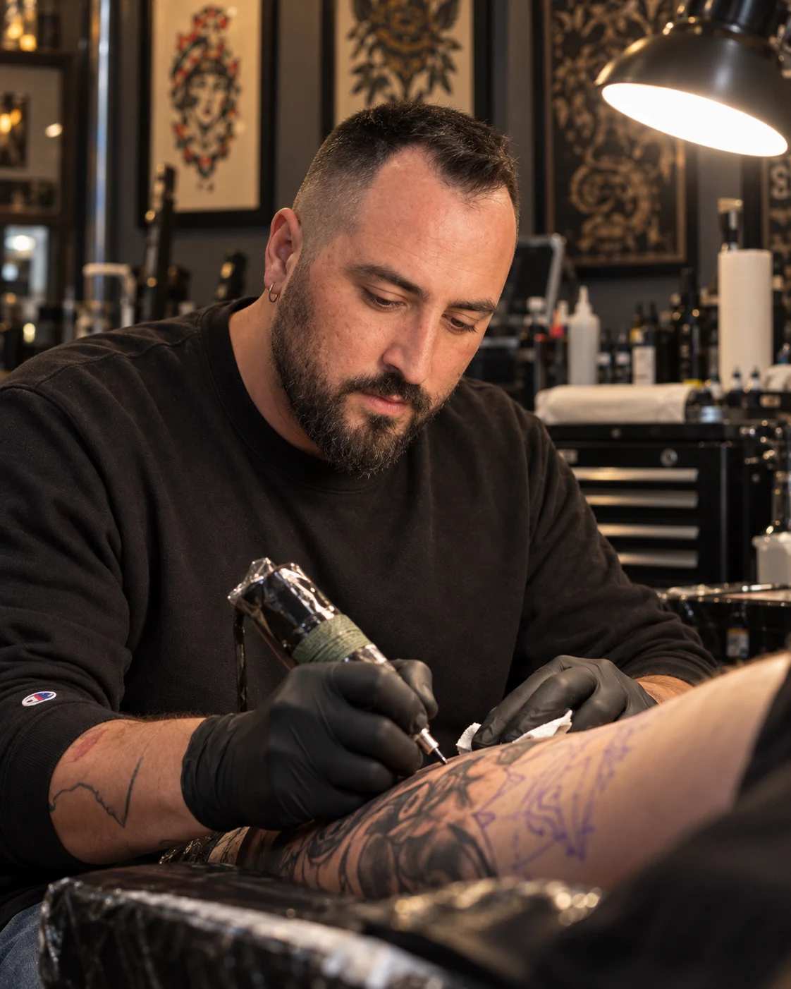 BORZ tatuando el brazo de un cliente en su estudio de Seattle, con guantes negros bajo una lámpara de trabajo cálida